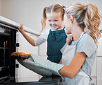 Mother holding tray of muffins. Happy woman taking tray of fresh, baked muffins from the oven. Little girl baking with her mother. Mother and daughter enjoying a tray of dessert muffins