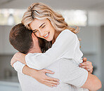 Beautiful woman hugging husband while smiling in their home. Young wife hugging her man while standing in the living room. Feeling happiness and love and showing affection. Husband and wife embracing