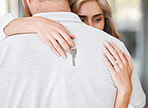 Closeup of happy wife hugging husband while holding keys after buying first home. Couple relocating to new house or apartment. Newlywed couple moving into their new place