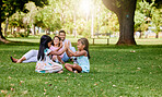 A happy asian couple lying together on grass outside, loving parents enjoy quality time with their little daughters playing a game. Couple bonding during family time at park with adopted foster sister