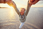 Father and daughter having fun at the beach. Parent swinging little girl around by the arms by the sea at sunset