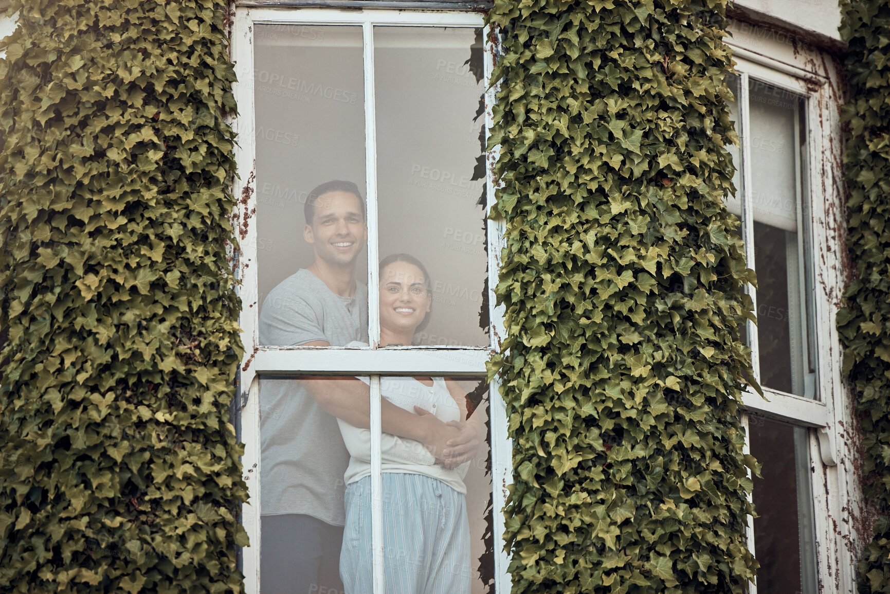 Buy stock photo Happy, hug and portrait of couple by window of hotel for romantic anniversary vacation in Amsterdam. Love, smile and young man and woman by glass door of holiday home with ivy plants, vines or leaves