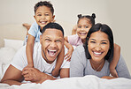 Portrait of a cheerful family lying together on bed. Little boy and girl lying on their parents laughing and having fun. Mixed race couple bonding with their son and daughter. Hispanic siblings enjoying free time with their mother and father