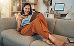 Full length smiling mixed race woman using credit card for ecommerce on digital tablet at home. Happy hispanic sitting alone on sofa, using technology for ebanking. Relaxing, ordering, buying online