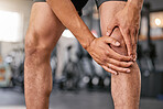 Closeup of one caucasian man holding his sore knee while exercising in a gym. Male athlete suffering with painful leg injury from fractured joint and inflamed muscles during workout. Struggling with stiff body cramps causing discomfort and strain