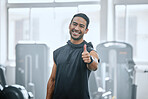 Portrait of smiling trainer alone in gym, showing thumbs up sign and symbol. Asian coach endorsing support after workout in exercise health club. Young happy man in fitness centre for routine training