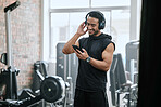 Smiling asian trainer alone in gym, listening to music on headphones from cellphone. Handsome coach standing in health club workout, selecting song from playlist on technology. Man in fitness centre