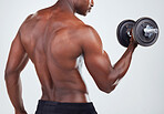 One young African American fitness model posing topless while exercising with dumbbells .Confident black male athlete isolated on grey copyspace while weightlifting in a studio