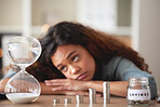 Young african american woman staring at an hour glass while looking bored at home. Mixed race person counting down while financial planning in her living room. Waiting for her investments and savings