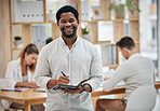 African business man writing in book, taking notes and planning his routine schedule while working in an office with colleagues. Portrait of a smiling, creative and black corporate professional 