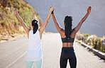 Rear view of two fit young sportswomen standing with their hands raised in the air together celebrating their victory after achieving fitness goals together. Two female athletes raising their arms up after exercising outdoors