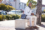 One happy african american man wearing headphones around his neck and texting on a phone while out in the city on his daily commute. A handsome black male smiling while checking his social media feed