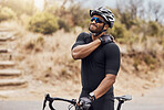 Fit hispanic young man touching his shoulder, experiencing a cramp. Young man taking a break from cycling for a neck and shoulder injury. Athletic man standing outside with his bike
