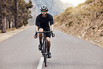 One athletic young man cycling outside. Sporty fit male wearing helmet and glasses while riding a bike on a road along the mountain for exercise. Endurance and cardio during a workout and training