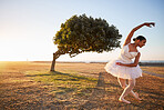 Young female ballerina dancing outside in nature environment with a tree in the background. Ballet dancer bowing in front of a bended tree