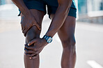 African american athlete taking a break from running to touch his knee and inspect an injury. Fit, sporty, healthy man feeling pain in his knee joint during a jog in the city. Athlete working out 