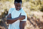 One handsome young african american male athlete suffering with an arm injury while exercising outdoors. Dedicated black man holding his shoulder in pain during his outdoor workout in nature