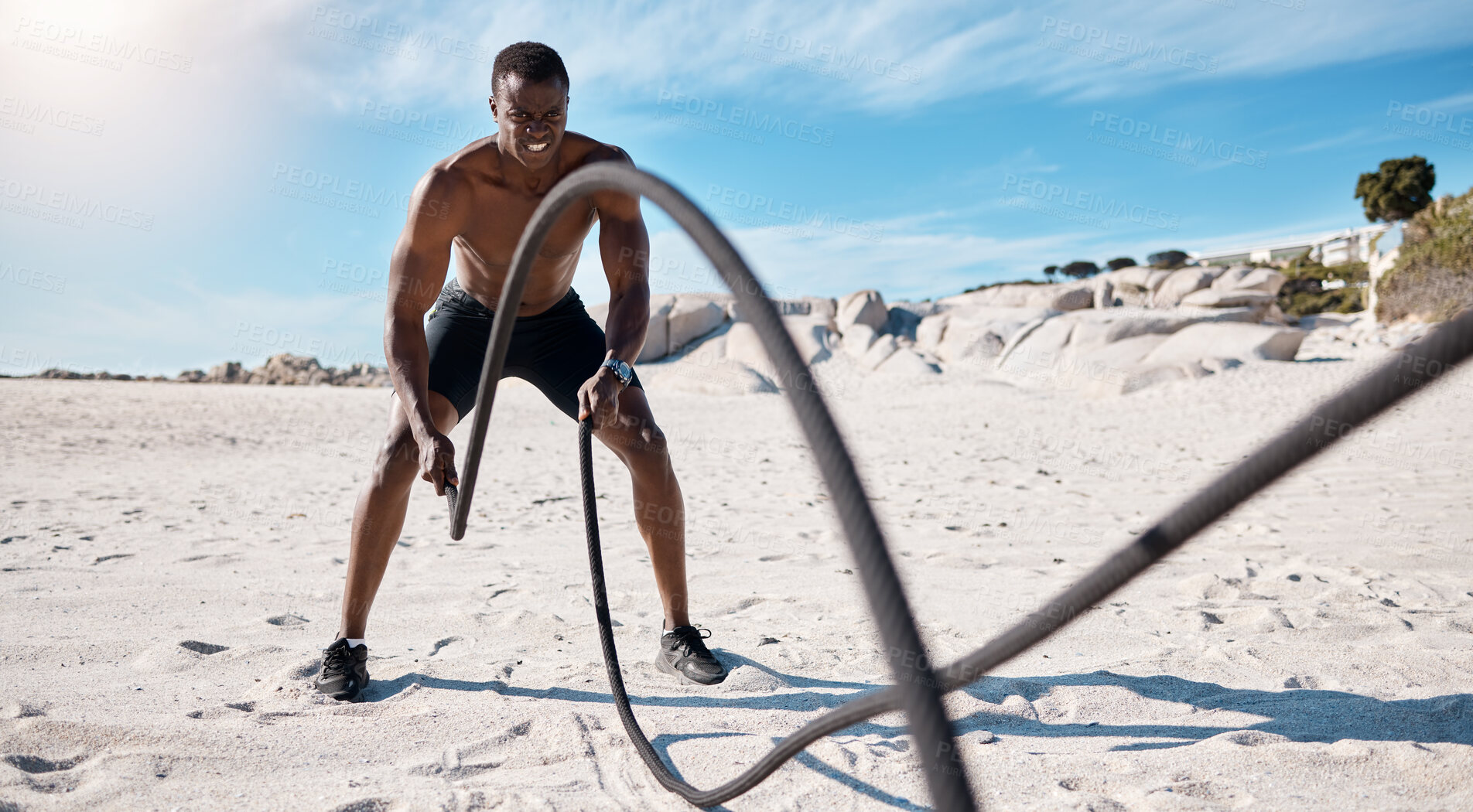 Buy stock photo Athlete, exercise and battle ropes on beach for fitness, workout and cardiovascular health outdoor. Black man, high intensity training by ocean and challenge with spiral and slam for strength