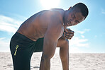 Fit young topless black man taking a break from his run or jog at the beach in the morning for exercise. One strong male bodybuilder athlete looking focused for his cardio and endurance workout