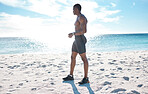 Fit young shirtless black man taking a break from his run or jog at the beach in the morning for exercise. One strong muscular male athlete looking focused for his cardio and endurance workout