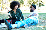 Interracial couple in nature park together, man and woman relax with drink on grass and happiness for people on picnic date outside. Happy black friends dating, laughing and having fun on weekend