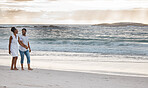 Cheerful african american couple spending a day at the sea together. Happy boyfriend and girlfriend holding hands while walking on the beach. Caring husband and wife bonding on the seashore