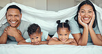 Portrait of happy family with two children lying under duvet smiling and looking at camera. Little girl and boy lying in bed with their parents bonding and having fun