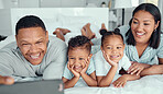 Cheerful father holding phone and taking selfie or recording funny video with his family. Happy mixed race family with two children and parents posing together for a family picture on a mobile phone