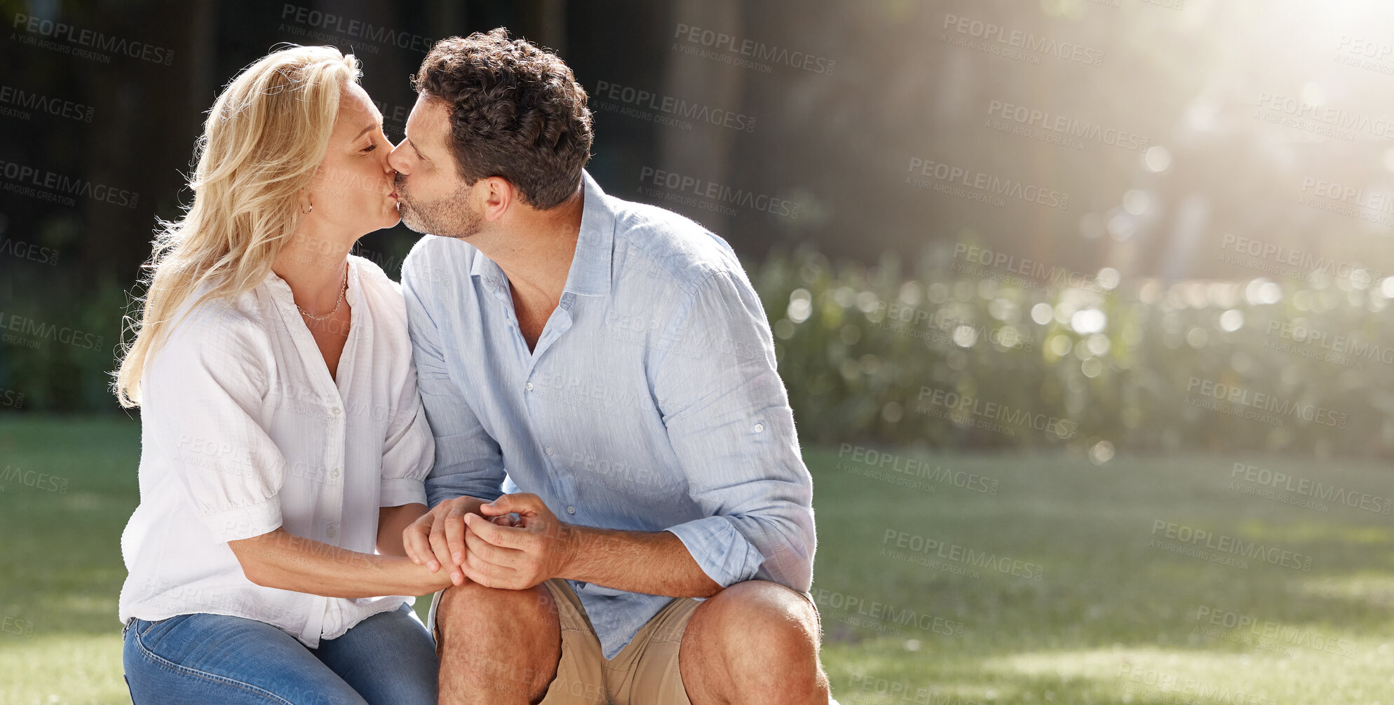 Buy stock photo Happy, couple and kiss with love outdoor for relationship romance, marriage anniversary and bonding in sunshine. Woman, man and affection with care, holding hands and commitment in garden for date