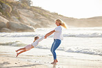 Happy mother and her adorable little girl having fun on the beach. Mom spinning little girl around while enjoying family time by the beach