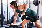 One fit young caucasian man doing single arm bent over rows on a bench with dumbbells while training in a gym. Focused guy challenging himself by lifting heavy weights to build muscle and endurance during a workout