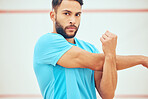 Portrait of mixed race squash player stretching and looking focused before playing a game on court. Fit active hispanic athlete standing alone and getting ready for training practice in sports centre