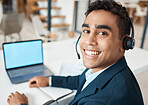 Portrait of a young happy mixed race businessman working on a laptop alone at work. One hispanic businessperson smiling while working at a desk in an office
