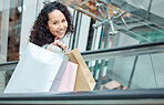 Portrait beautiful mixed race woman standing on an escalator while shopping in a mall. Young hispanic woman carrying bags, spending money, looking for sales and getting in some good retail therapy