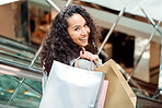 Portrait beautiful mixed race woman standing on an escalator while shopping in a mall. Young hispanic woman carrying bags, spending money, looking for sales and getting in some good retail therapy