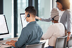 Hispanic call centre telemarketing agent from the back talking on a headset while working on a computer in an office alongside his colleagues. Busy consultants operating a helpdesk for customer service and sales support