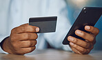 Closeup hands of african man using a phone while holding his credit card. African american business man shopping online while working late at night at his work. Putting in overtime after hours