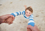 Happy caucasian boy swinging and spinning in circles by the arms at the beach shore with his father. Face of cute playful kid having fun while bonding with a parent on sunny summer vacation outdoors