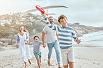 Happy caucasian parents and kids playing with a toy plane while enjoying quality time on a relaxing fun family summer vacation together at the beach. Loving mom and dad bonding with cheerful sons