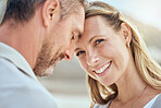 Happy and loving mature caucasian couple enjoying a romantic date at the beach together on a sunny day. Cheerful affectionate wife standing face to face and heads touching with husband while bonding on vacation outdoors