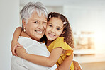 Portrait of mixed race grandmother and granddaughter hugging in living room at home. Smiling hispanic girl embracing senior grandparent and bonding in lounge. Happy elderly woman and child together