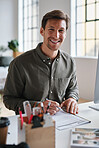 Happy businessman smiling sitting at desk in office holding pen