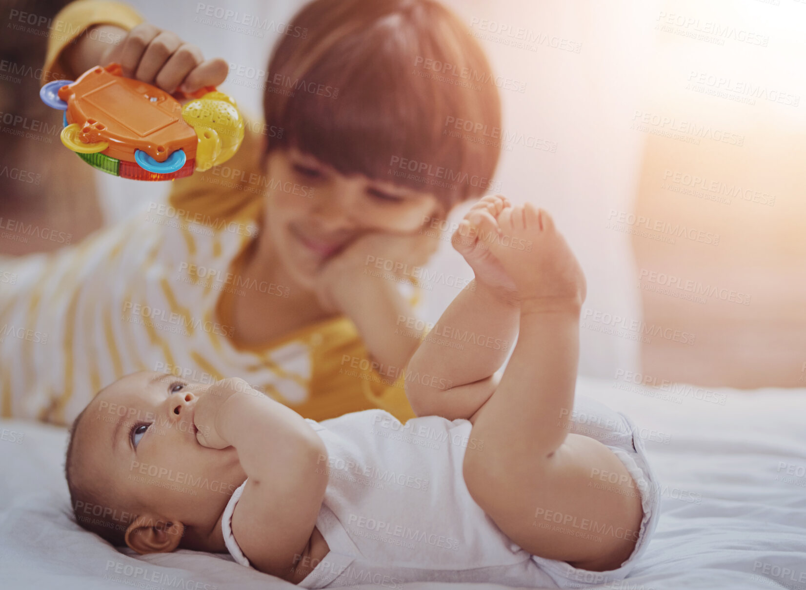 Buy stock photo Siblings, baby and playing with toy on bed for bonding, fun activity and motor skills development in home. Family, brothers and curious child with plastic rattle for entertainment and love in bedroom