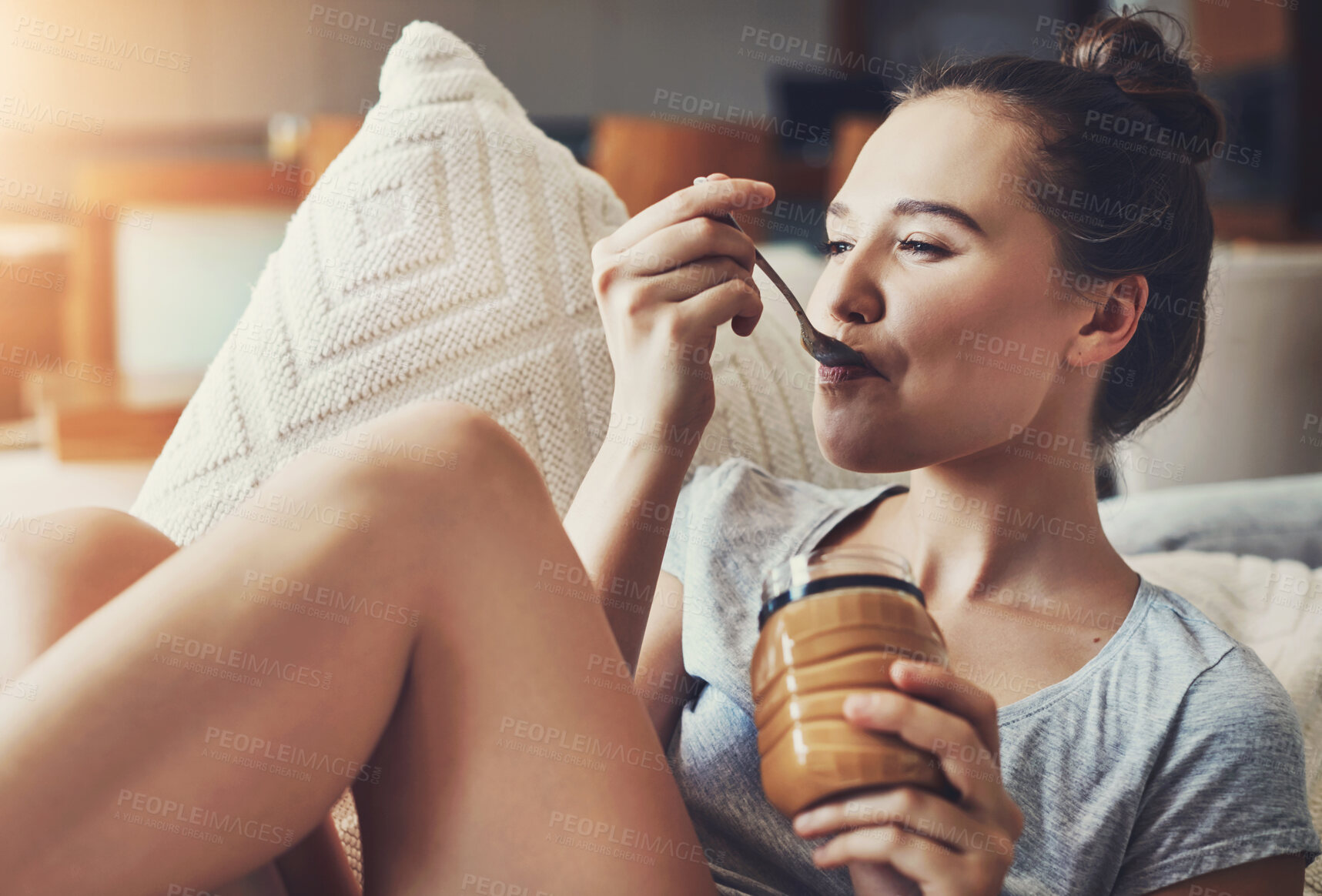 Buy stock photo Woman, smile and eating peanut butter in home with jar, health and vegan diet for wellness on couch. Female person, food nutrition and spoon with nut spread, protein snack and breakfast on sofa