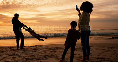 Buy stock photo Family, sunset and fun on beach vacation together, people and father swinging child for bonding in summer. Mother, smartphone and capture picture or memory, love and silhouette or sky background