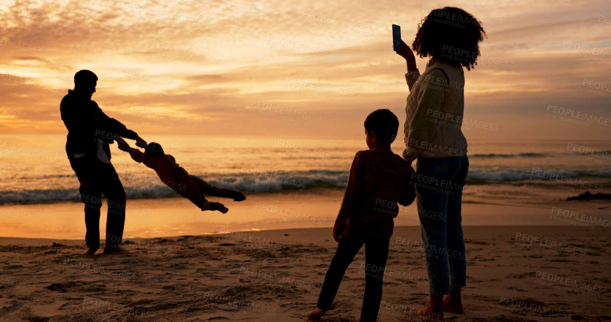 Buy stock photo Family, sunset and fun on beach vacation together, people and father swinging child for bonding in summer. Mother, smartphone and capture picture or memory, love and silhouette or sky background