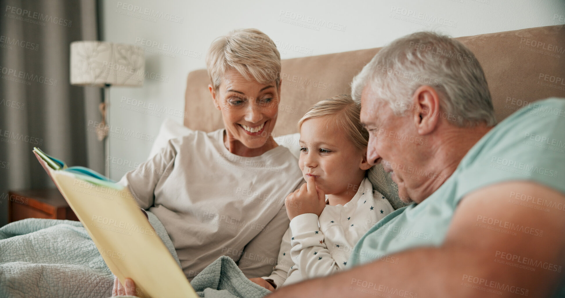 Buy stock photo Grandparents, girl and reading book in bed for fairytale, literature and bonding at sleepover. Home, grandchild and people learning together for love, language and grandma or grandpa for bedtime