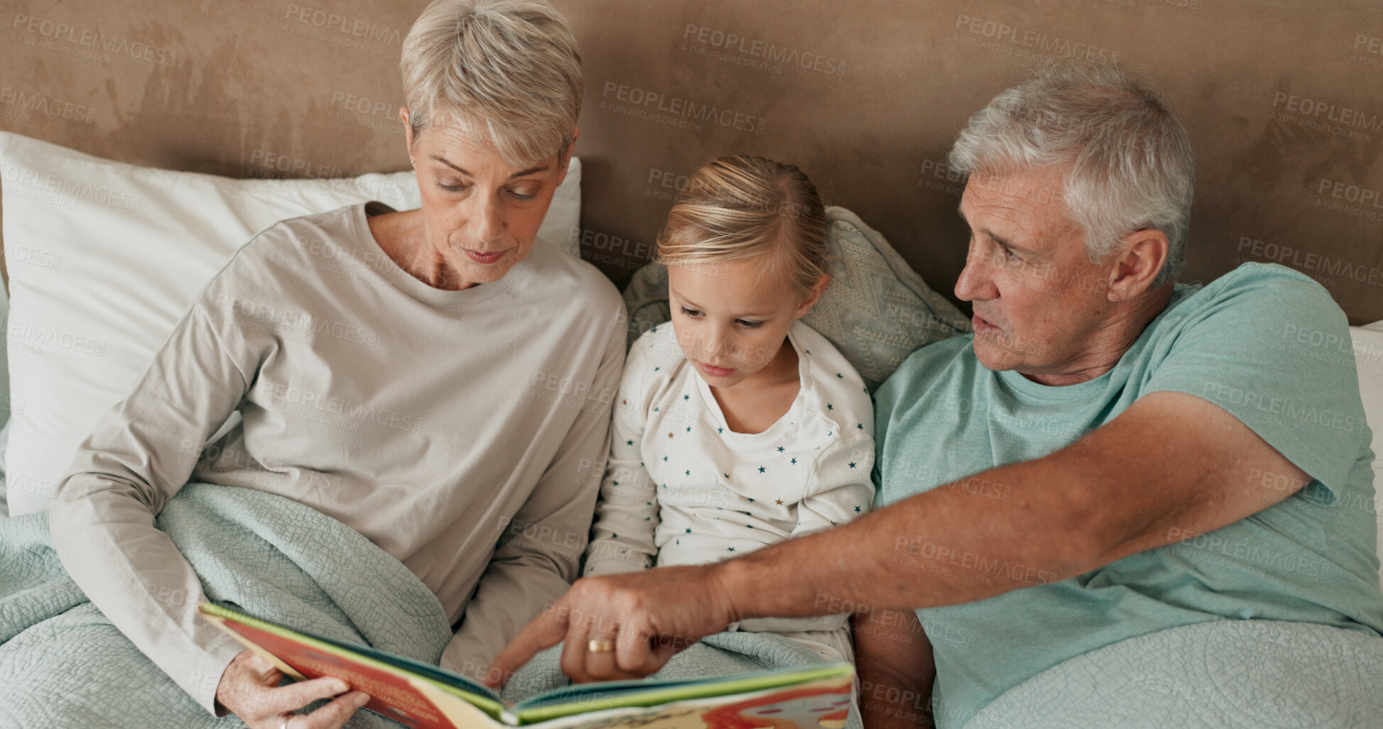 Buy stock photo Grandparents, girl and reading fiction in bed for storytelling, literature and bonding at sleepover. Home, grandchild and people learning together for love, book and grandma or grandpa for fairytale