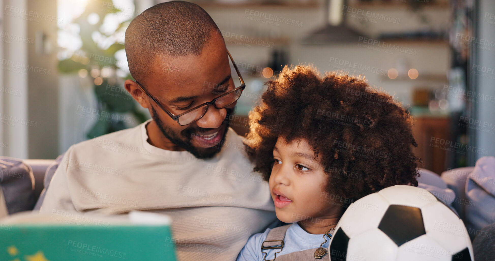 Buy stock photo African man, son and reading book on sofa with soccer ball, listening and bonding in family house. Storytelling, father and boy with listening, fantasy or relax with literature for learning in lounge