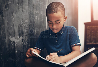 Buy stock photo Shot of a young boy writing in a book while sitting at home